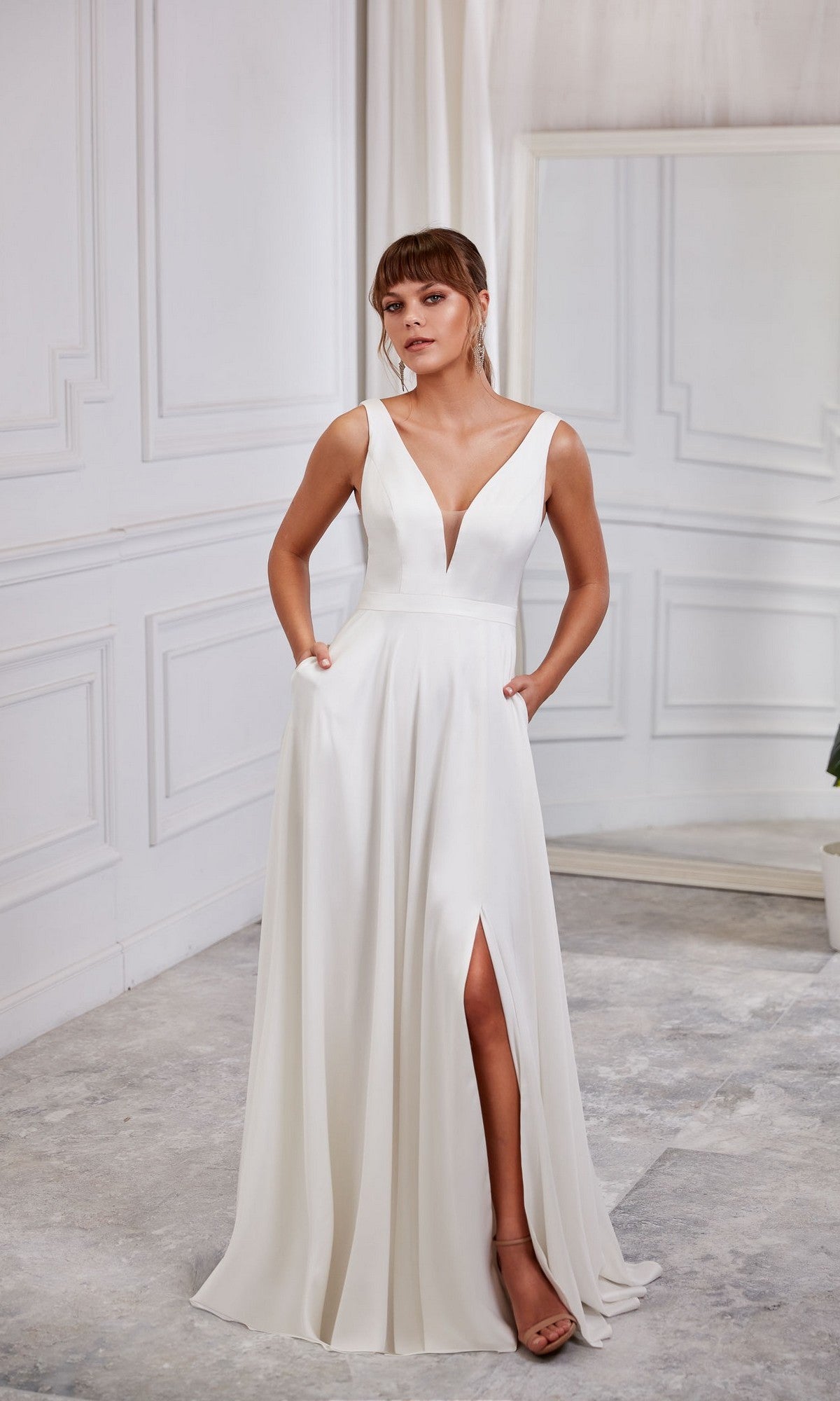 A woman wears the Aerie Couture 2007 Long White Dress, a sleeveless A-line formal dress with a deep V-neckline and thigh-high slit, standing in a minimalist white room.